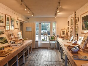 An art gallery with wooden floors and walls, displaying framed artworks on easels and shelves.