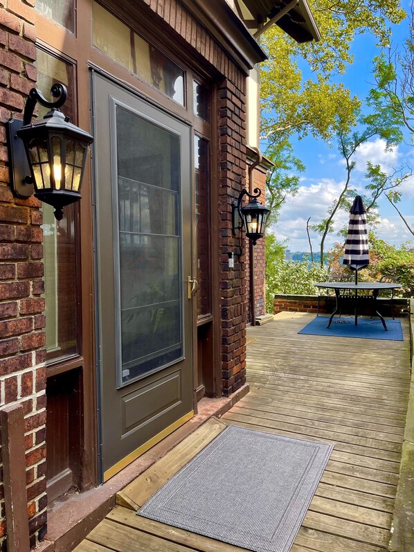 A brick house with a dark front door, two wall-mounted lanterns, and a deck with a striped umbrella.