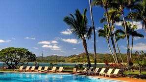 A swimming pool with lounge chairs, palm trees, and a view of the ocean and hills. - Lae Nani 313, Great View Ground Floor (Kapaʻa)