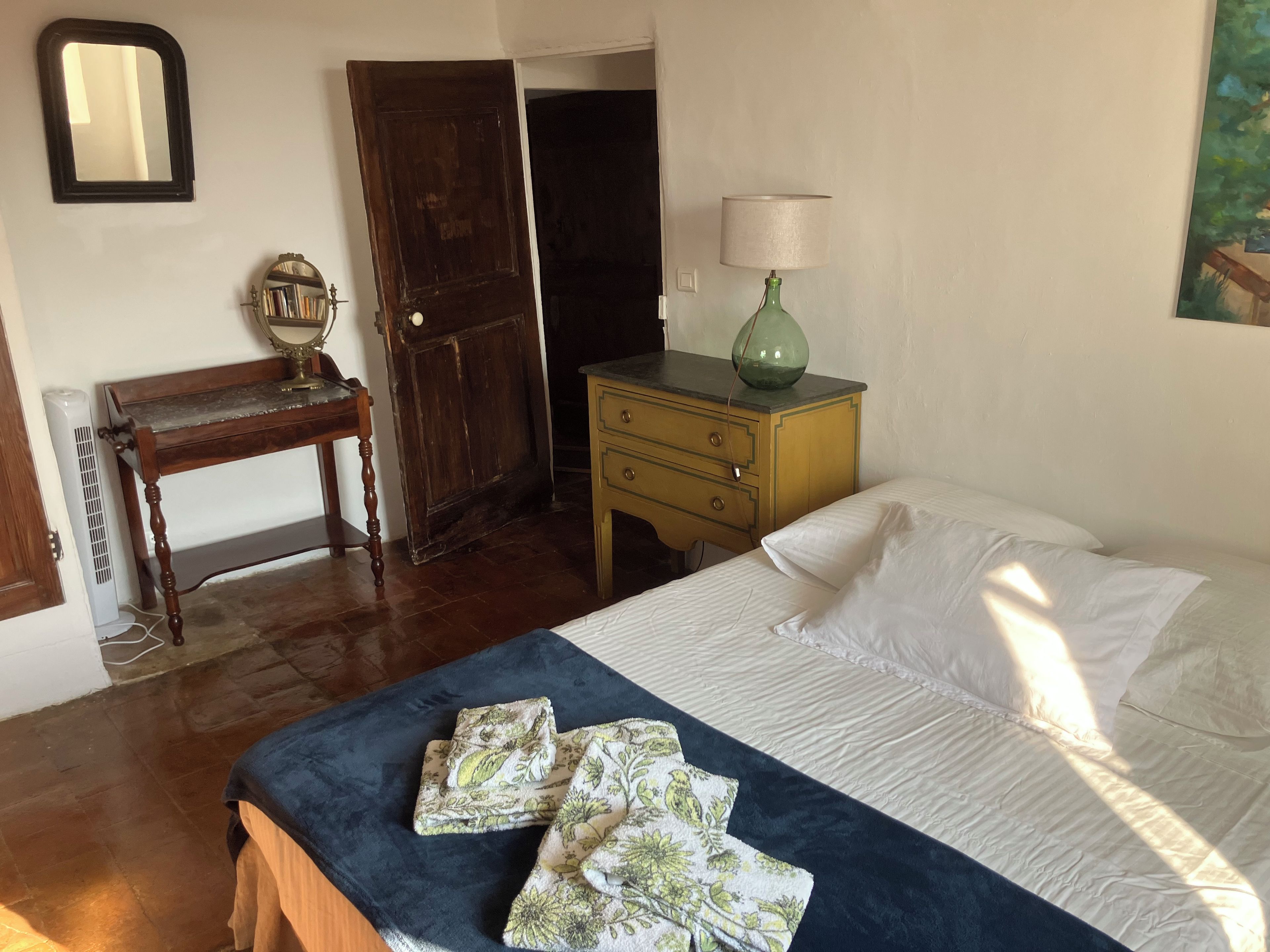 Une chambre à coucher comprenant un lit, une table de chevet, une commode, une chaise en bois, un miroir et une porte.