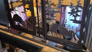 Une pièce avec un plafond en bois, une cloison en métal noir ornée de découpes représentant un cerf et un cheval, et un mur en pierre en arrière-plan.