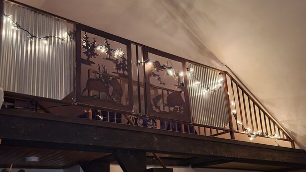 Un escalier en bois orné d’une rampe décorative, une horloge murale et une fenêtre avec des stores.