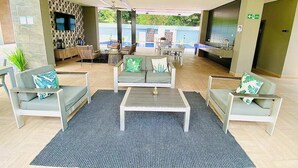 Ein überdachter Außenbereich mit Sofas und einem Couchtisch, einem an der Wand montierten Fernseher und einem Pool im Hintergrund.