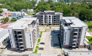 Un moderno complejo de apartamentos con varias construcciones, un patio central y una zona de estacionamiento.