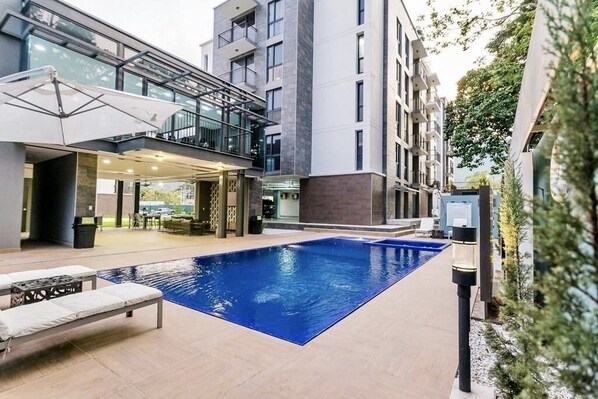 Un edificio moderno con piscina, zona de estar exterior y un área cubierta con mesas y sillas.