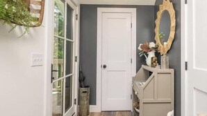 Un couloir avec une porte blanche, un tapis à motifs, un banc en bois et un miroir décoratif.