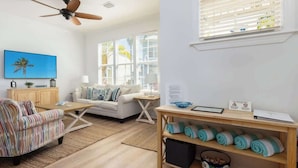 A well-lit living room with a sofa, armchair, and coffee table. There are windows with blinds, a ceiling fan, and a TV on the wall. - Oceanside Anglers Reef Home+Beach, Pool and Kayaks (Islamorada)