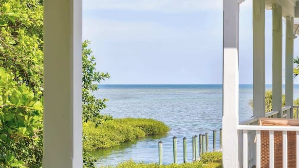 A balcony with a view of the ocean, surrounded by greenery and a white railing. - Oceanside Anglers Reef Home+Beach, Pool and Kayaks (Islamorada)