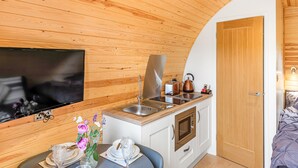 Cocina compacta con techo de madera, horno empotrado, un lavabo y un televisor montado en la pared.