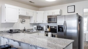 Una cocina moderna con gabinetes blancos, encimera de granito, electrodomésticos de acero inoxidable y una cafetera.
