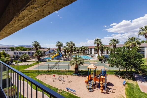 Guests can enjoy a playground with slides and swings surrounded by lush greenery and palm trees, with a tennis court nearby.