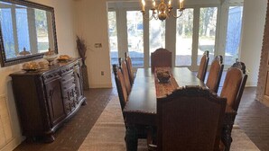 Een eetkamer met een lange tafel, stoelen, een kroonluchter en een grote spiegel aan de muur.