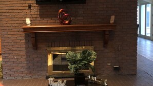 Een woonkamer met een bakstenen muur, een flatscreen televisie boven een open haard en een bijzettafeltje met een plant.