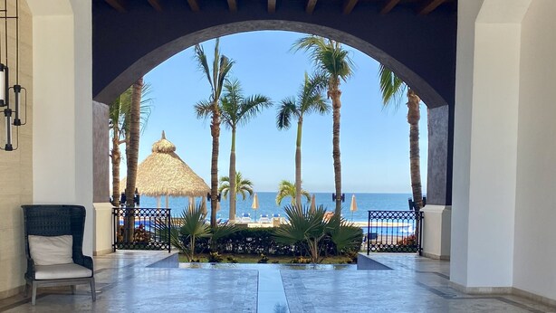 A pool area with a view of the sea, palm trees, and a thatched-roof structure. - BEACHFRONT 2 BEDROOM CONDO IN LAS GAVIAS RESORT - Sleeps 6 (Mazatlán)