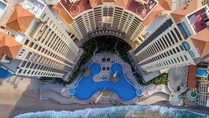An aerial view of a hotel with multiple balconies, a central pool area, and a beachside location. - BEACHFRONT 2 BEDROOM CONDO IN LAS GAVIAS RESORT - Sleeps 6 (Mazatlán)