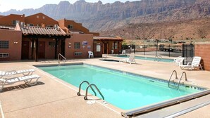 Ein Poolbereich mit mehreren Pools, Liegestühlen und einem Gebäude mit einem Ziegeldach.
