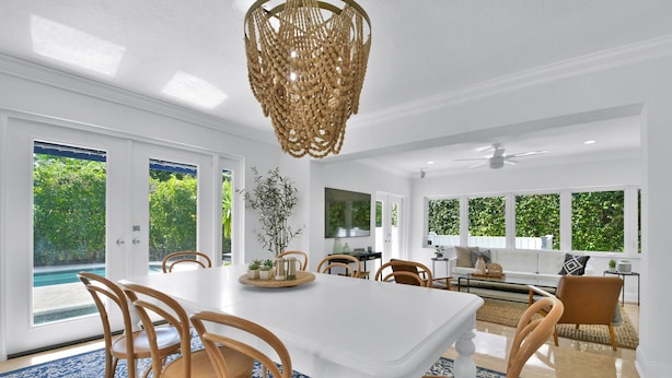 A spacious dining area with a white table, wooden chairs, and a blue patterned rug.