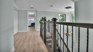 A hallway with a wooden floor, a white door, and a blue chair in the background.