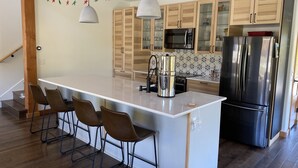 Une cuisine moderne dotée d’un îlot central, de tabourets de bar, d’appareils électroménagers en acier inoxydable et de meubles de rangement en bois.