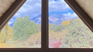 Une pièce dotée d’un plafond triangulaire et de deux fenêtres donnant sur un paysage de montagnes et sur les couleurs automnales des arbres.