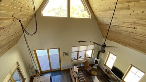 Une pièce de style « loft », avec un plafond haut, des poutres en bois, un coin repas comprenant une table et des chaises en bois, un canapé et un ventilateur de plafond.