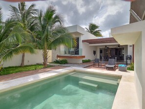 A modern outdoor pool area with a patio, seating, and a view of the house.