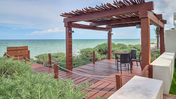 A wooden deck with a pergola, overlooking a beach. - Casa Kux  -  Yucatan Home Rentals (Chicxulub Puerto)