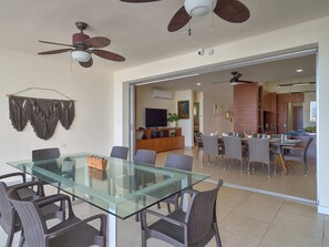 A modern dining area with a glass table and chairs, a ceiling fan, and a kitchen visible through an open door.