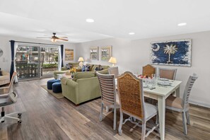 A spacious living area with a dining table set for four, a sofa, and a chair with a woven backrest.
