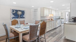 Un coin repas avec une table dressée pour quatre personnes, une cuisine avec des meubles blancs et une œuvre d’art accrochée au mur.