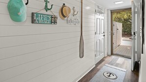 Un couloir avec une porte donnant sur un patio, un porte-chapeaux fixé au mur et un paillasson.