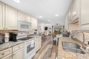 A kitchen with white cabinets, a granite countertop, a stainless steel sink, and a built-in microwave.