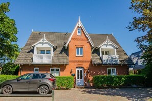 A two-story house with a red brick facade, a grey roof, and a small balcony on the second floor.