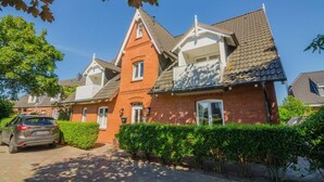 A row of brick houses with a central red building, a car parked in front, and a well-maintained hedge. - Senwai-Hüs, Whg. 1 Braderup - Senwai-Hüs (Sylt)