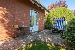 A brick house with a small patio, a table with chairs, and a blue-striped outdoor seating area. - Senwai-Hüs, Apartment 1, Braderup - Senwai-Hüs (Sylt)