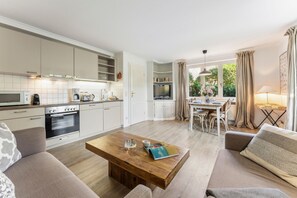 A modern kitchen with built-in appliances, a dining area with a table and chairs, and a cozy seating area with a sofa and a coffee table. - Senwai-Hüs, Apartment 1, Braderup - Senwai-Hüs (Sylt)