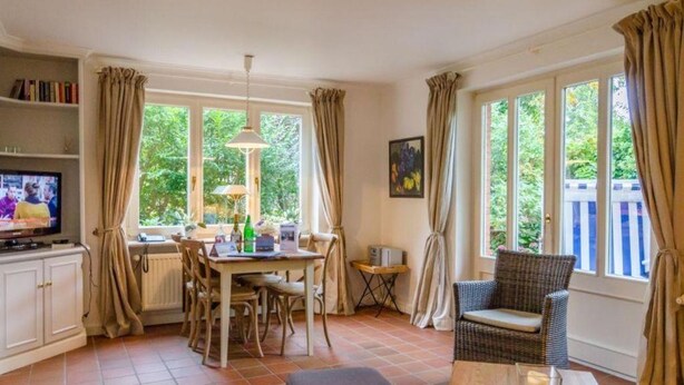 A cozy living room with a dining area, a television, and large windows with curtains. - Senwai-Hüs, Whg. 1 Braderup - Senwai-Hüs (Sylt)
