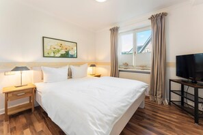 A hotel room with a bed, bedside lamps, a television, a window with curtains, and a painting on the wall.