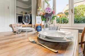 A dining table set with plates, glasses, and cutlery, a vase with flowers, and a bottle of wine.