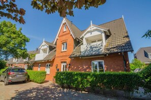 A row of brick houses with a central red building, a car parked in front, and a well-maintained hedge. - Senwai-Hüs, Apartment 1, Braderup - Senwai-Hüs (Sylt)