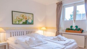 A hotel room with a large bed, two bedside tables with lamps, a window with curtains, and a painting on the wall. - Senwai-Hüs, Whg. 1 Braderup - Senwai-Hüs (Sylt)