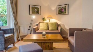 A cozy living room with a sofa, armchair, and a coffee table. There are two framed pictures on the wall and a lamp on the sofa. - Senwai-Hüs, Whg. 1 Braderup - Senwai-Hüs (Sylt)