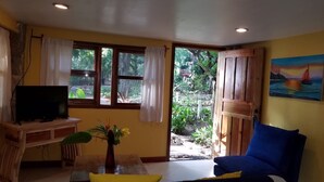 Quarto com televisão sobre suporte de madeira, uma cadeira azul, uma mesa amarela e um quadro de um veleiro na parede.