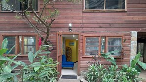 Uma casa de madeira com um sofá azul na entrada, rodeada por plantas.
