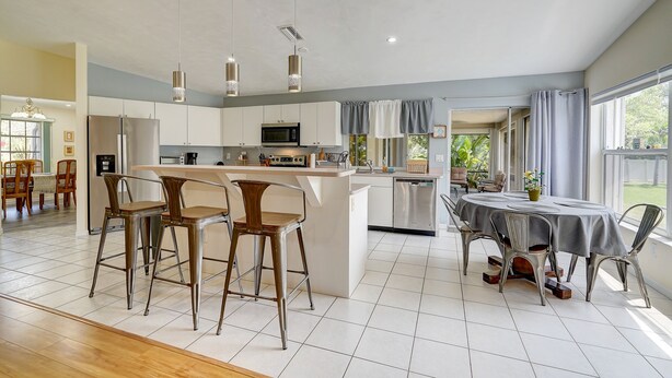 Een moderne keuken met een centraal eiland, barstoelen en een eettafel met stoelen.