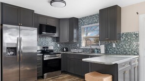 A modern kitchen with dark cabinets, stainless steel appliances, a microwave, and a hexagonal tile backsplash. - 3 Bedroom Mimosa Pool Oasis, Sleeps 8, Outdoor Shower &Hot Tub.Dog & EV Friendly (Cape May)