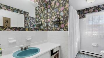 Une salle de bain avec un lavabo bleu, des carreaux blancs, un papier peint à motifs floraux et un espace douche.