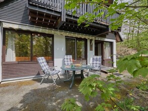 A modern house with a balcony, large windows, and a patio area with chairs and a table.