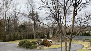 A residential driveway with a parked car, surrounded by trees and a grassy area. - Roomy 2 Bedroom Apt. w/en Suite BA, Private Entry & Parking, Tennis Court (Bethesda)