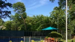 A backyard with a patio, a table and chairs, a green umbrella, and a flagpole with an American flag. - Roomy 2 Bedroom Apt. w/en Suite BA, Private Entry & Parking, Tennis Court (Bethesda)
